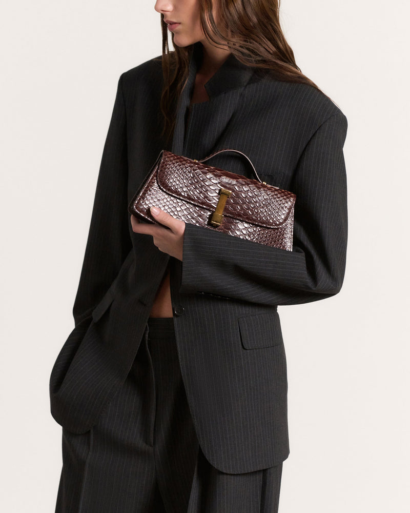 Kassandre Colonne clutch in brown python-effect leather with gold hardware, worn view